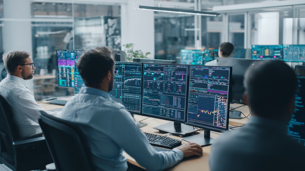 Blockchain developers collaborating in a modern office with multiple screens displaying blockchain data and performance metrics for optimization strategies.