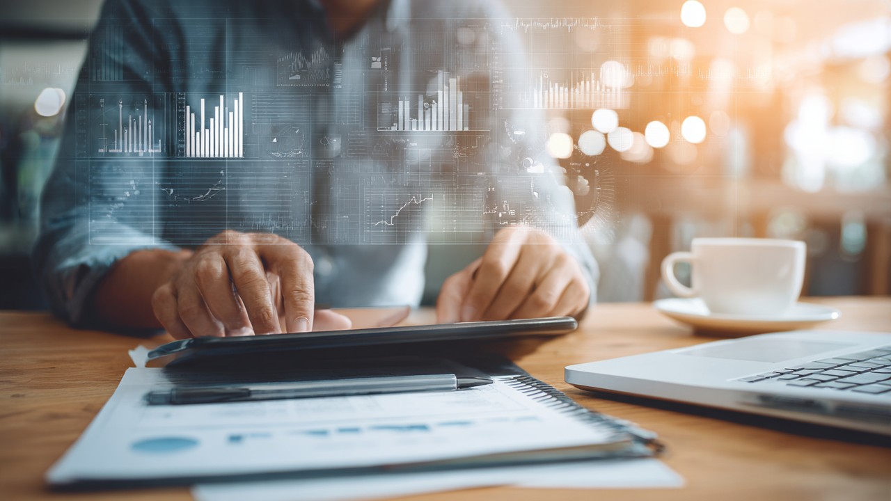 Professionnel d'affaires analysant des graphiques sur tablette et ordinateur portable dans un bureau lumineux, symbolisant la planification stratégique en infrastructure technologique.