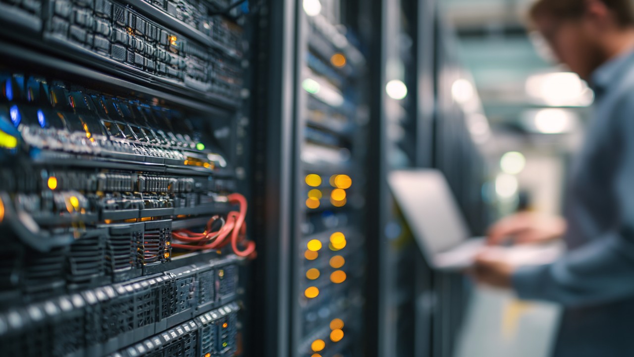 Close-up of a modern server room with blinking indicator lights and cables, system administrator managing servers on a laptop.