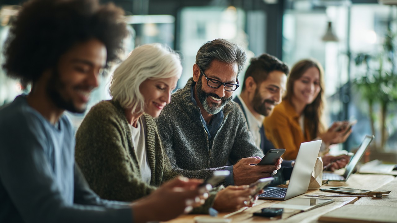 Diverse group of people using laptops, tablets, and smartphones in a modern office, engaging with websites and digital content.
