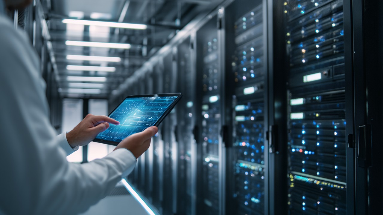 Modern data center with server racks, glowing lights, and technician monitoring performance on a tablet, showcasing infrastructure.