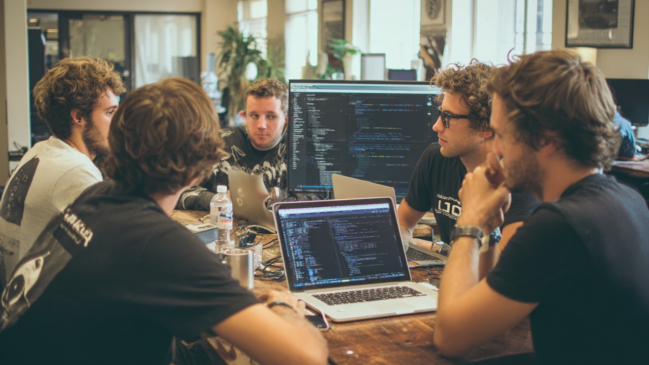 Groupe de développeurs logiciels collaborant autour de laptops avec code visible, dans un espace créatif, illustrant le travail d'équipe en intégration de frameworks PHP modernes.