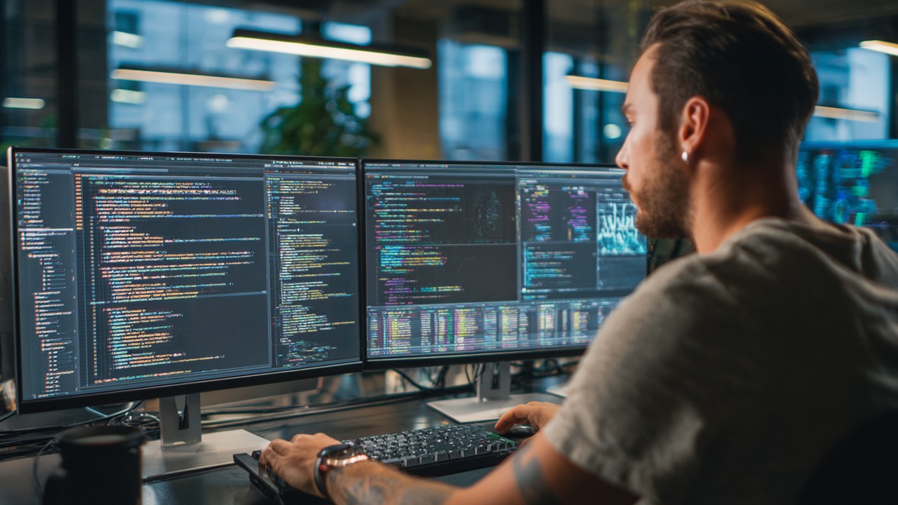 Realistic stock photo of a software developer analyzing PHP code and memory usage graphs on multiple monitors in a modern office.