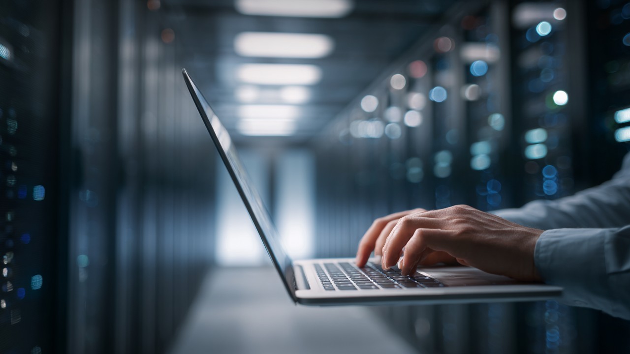 System administrator configuring server settings on a laptop in a data center with racks of servers, optimizing performance and reducing latency.
