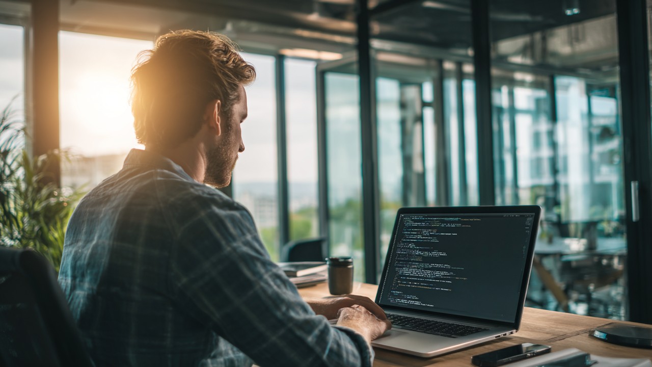 Focused software developer coding PHP on laptop in modern office with natural light, clean desk, emphasizing web development efficiency.