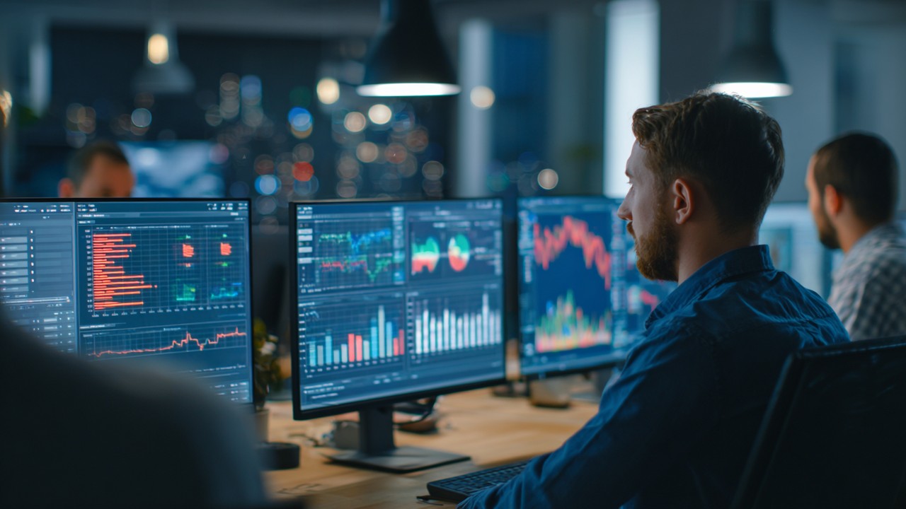 Office scene with IT support team analyzing server performance data on multiple screens, featuring charts and graphs for troubleshooting.