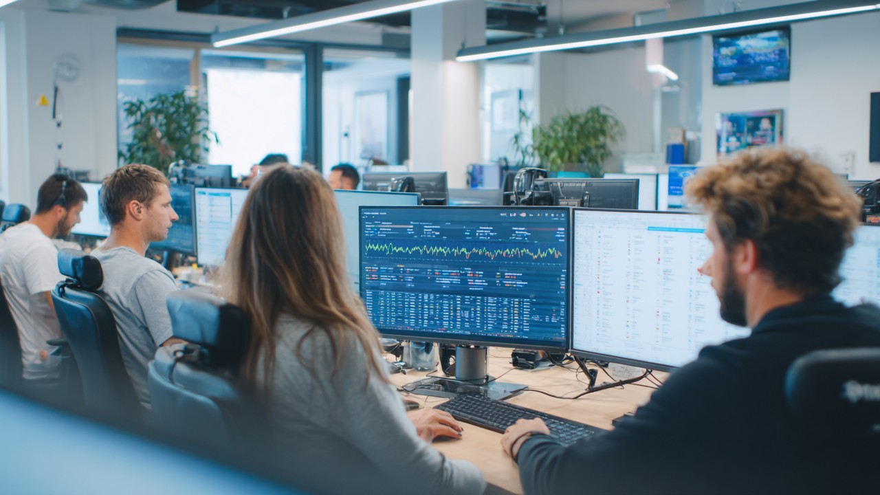 alt id: Tim tim pengembang dan administrator sistem bekerja sama di kantor modern dengan monitor menampilkan dashboard performa server dan kode PHP, fokus pada pengoptimalan kecepatan dan skalabilitas aplikasi.