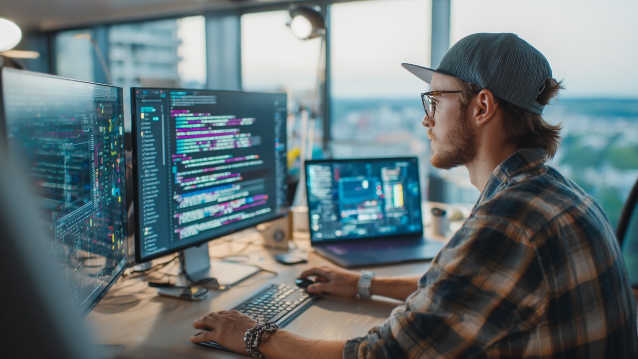 Web developer working on front-end code on a laptop with multiple screens showing web design and loading animations in a bright, creative workspace.
